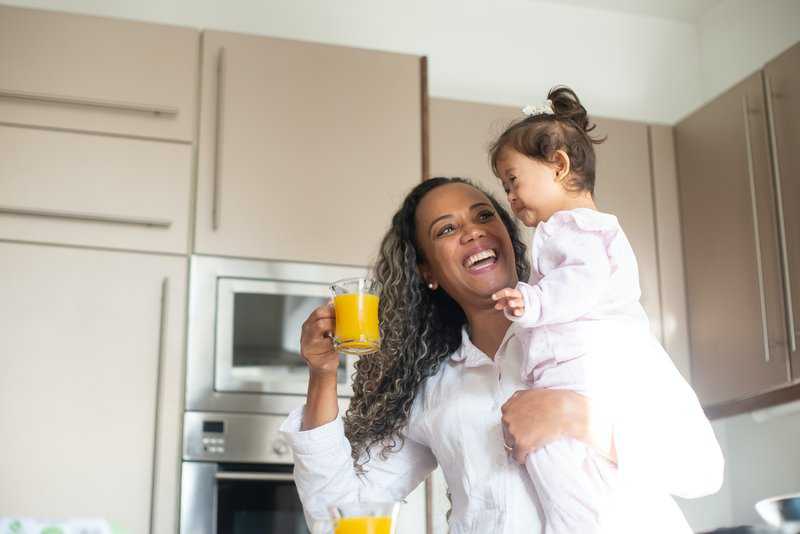 Mother and young child enjoying orange juice together in a bright kitchen.