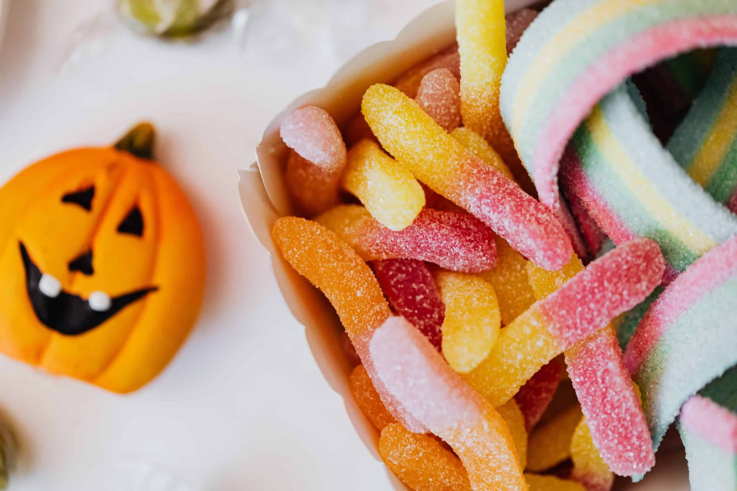 Halloween candy display with jack-o'-lantern decoration and colorful sour gummy candies on white surface.