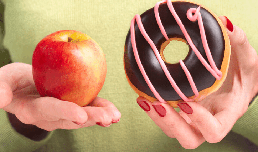 Hands holding red apple and chocolate donut, representing healthy versus unhealthy food choices for children.