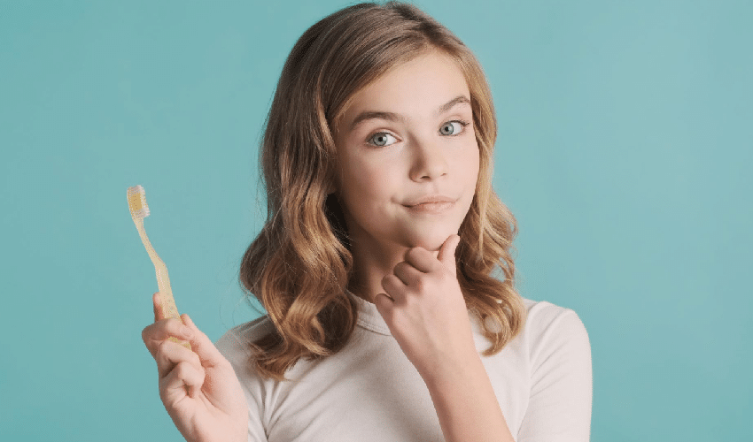 Woman holding toothbrush with thoughtful expression against blue background, dental care concept.