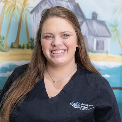 Smiling female staff member in dark scrubs with practice logo, professional headshot in dental office setting.