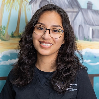 Smiling female dental professional wearing glasses and dark uniform in pediatric dental office setting.