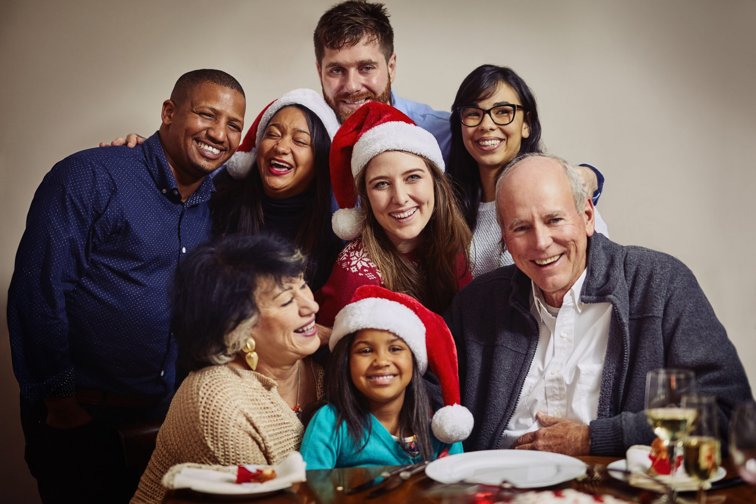 Family smiling together during a Christmas celebration, wearing Santa hats and enjoying time around the holiday table