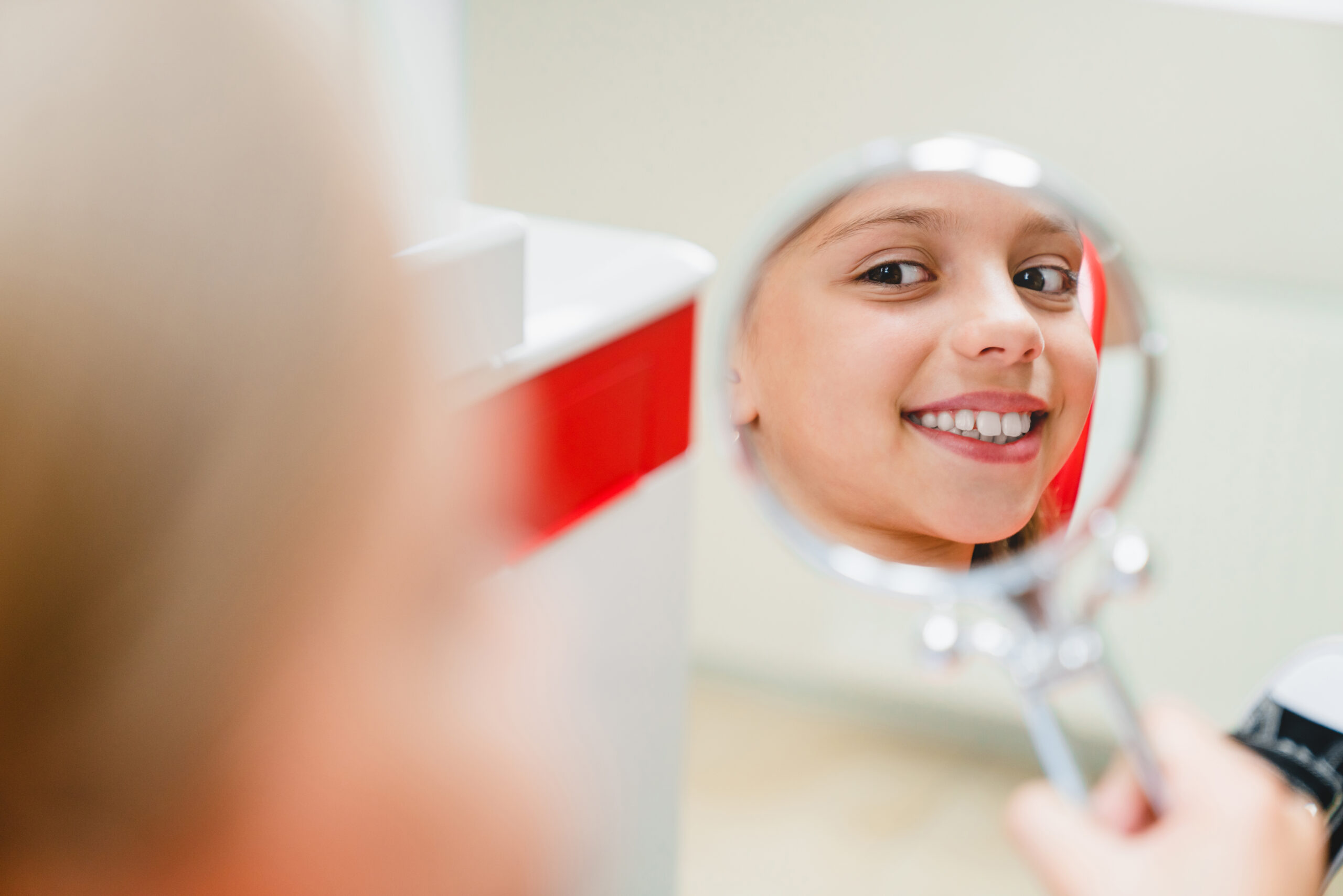 Smiling child looking at her teeth in a mirror during an orthodontic visit at a dental clinic