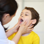 Pediatric dentist examining young child's mouth during dental checkup in clinical setting.