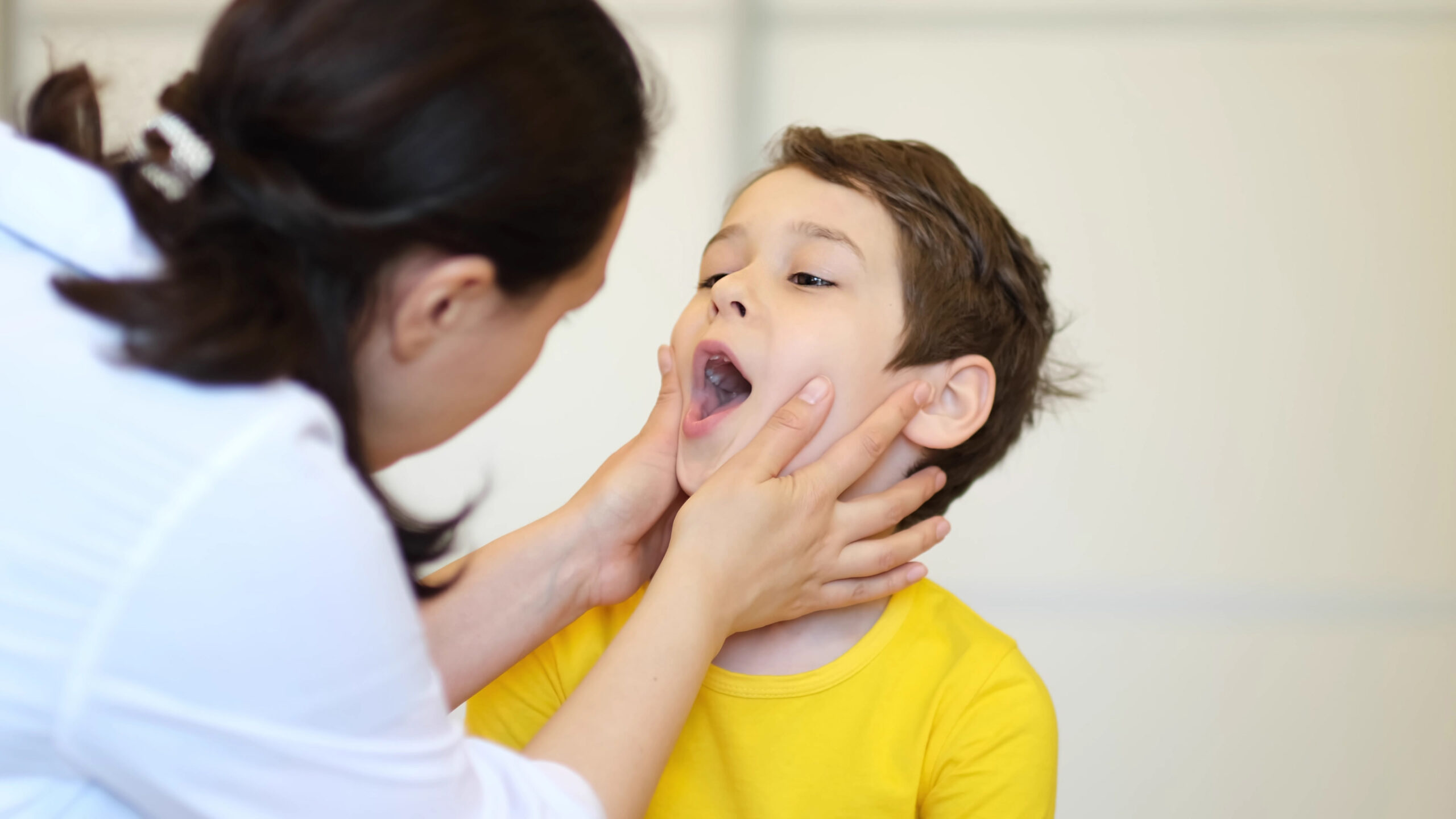 Pediatric dentist examining young child's mouth during dental checkup in clinical setting.
