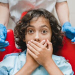 Nervous child covering mouth while sitting in a dental chair during a pediatric dental visit