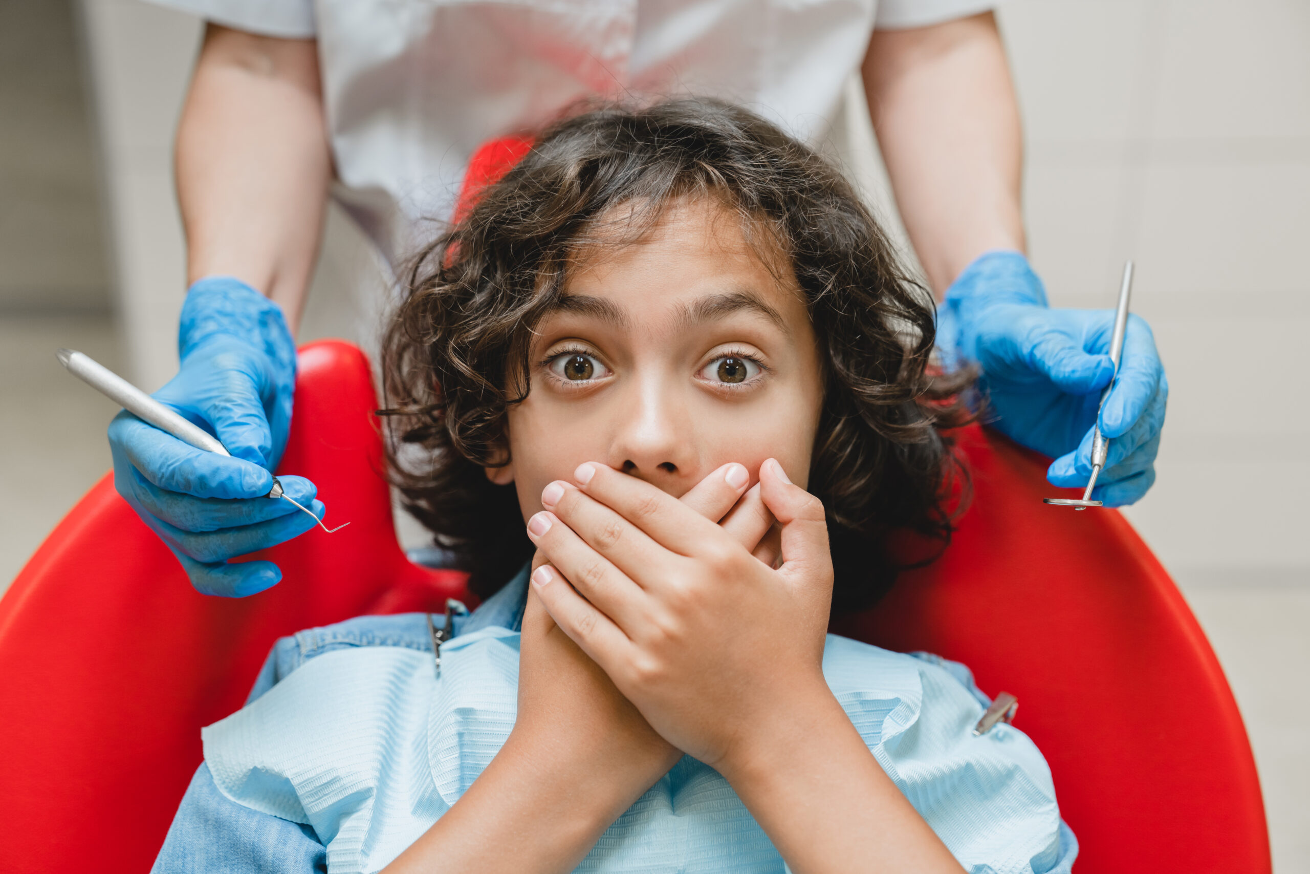 Nervous child covering mouth while sitting in a dental chair during a pediatric dental visit