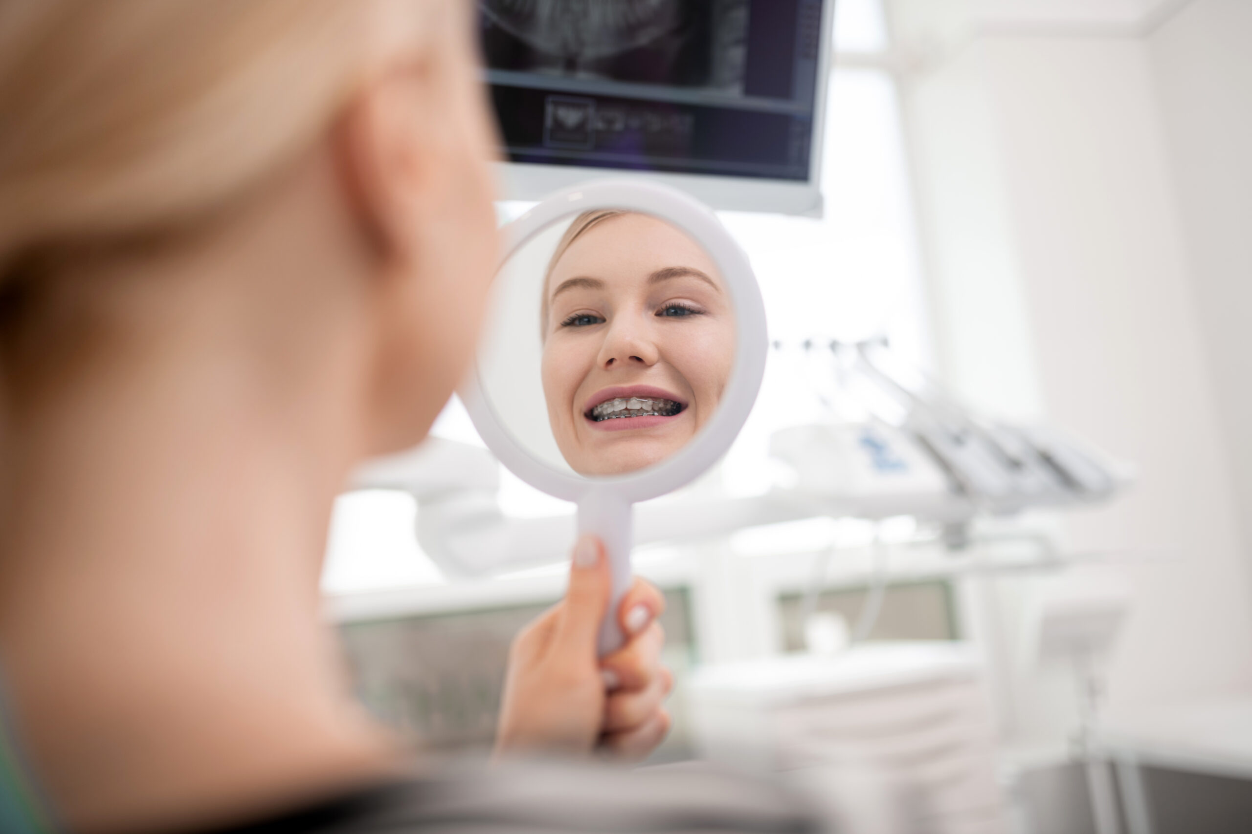 Teen smiling while checking her braces in a hand mirror during an orthodontic consultation